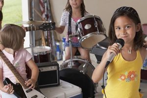 Girl Singing Into Microphone With Friends Playing Musical Instru